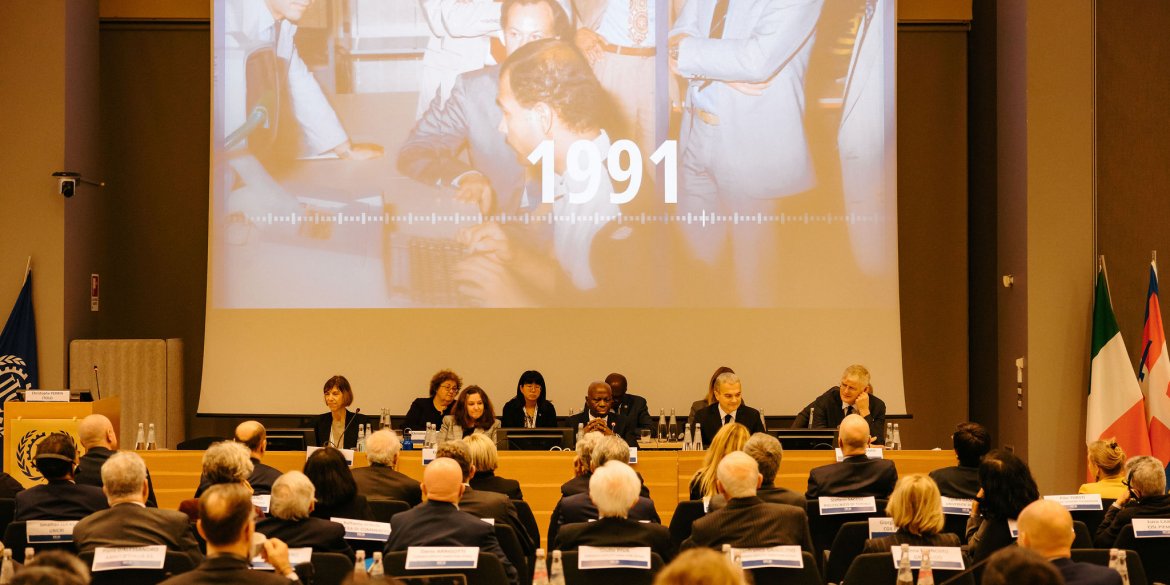 plenary view of the itcilo 60th anniversary proceedings in a large room with a panel of people and a screen and an audience